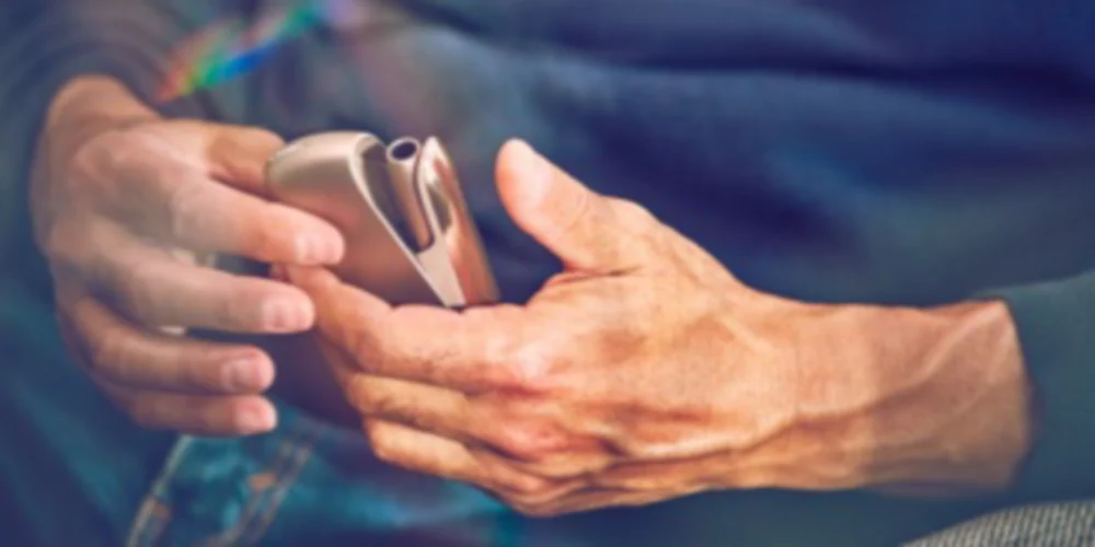 A woman holding an IQOS device looking at a laptop.