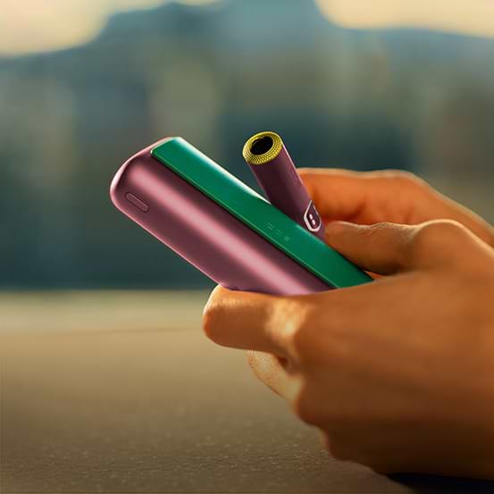 Hand holding IQOS Originals Duo holder and pocket charger in turquoise color.