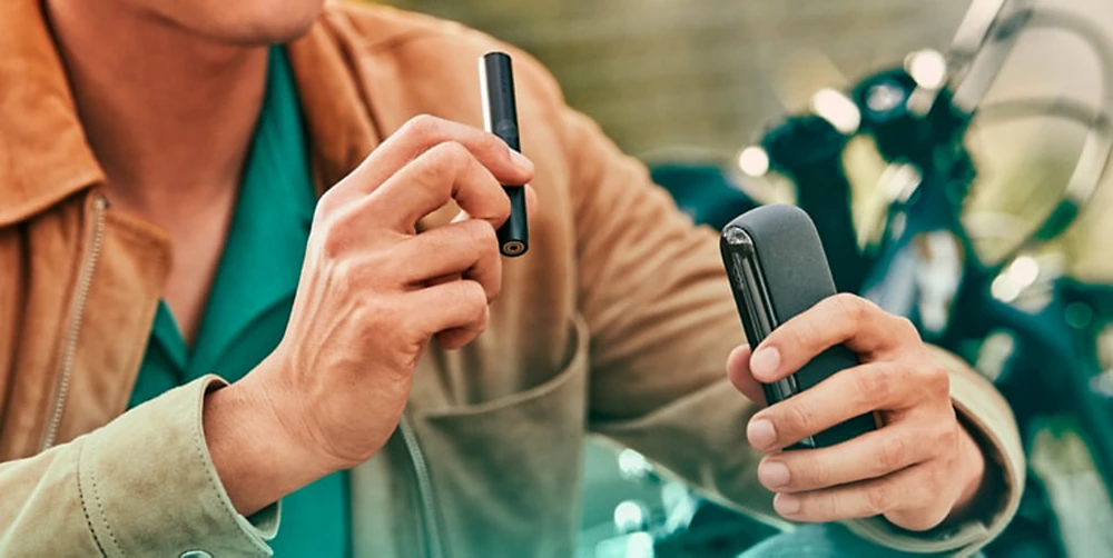 A person holding an IQOS ILUMA Pocket Charger and Holder. 