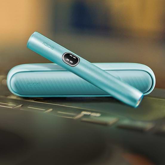 Turquoise IQOS Originals One device on a coffee table next to coffee cup.