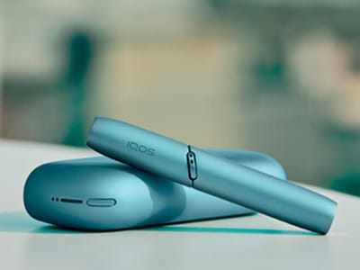 Laptop next to turquoise IQOS ORIGINALS DUO pocket charger.	 	 	