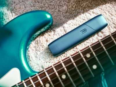 IQOS Originals One heated tobacco device, next to a turquoise guitar.