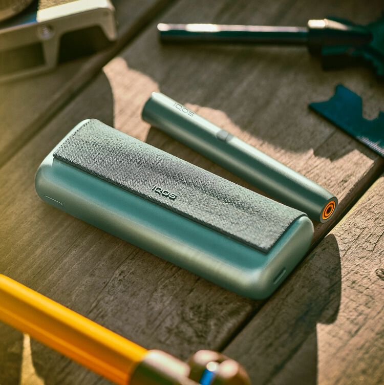 Close up of woman taking jade green IQOS ILUMA Prime device from holder.