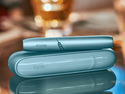 Laptop next to turquoise IQOS ORIGINALS DUO pocket charger.