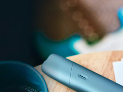 Blond woman checking her phone with a IQOS device on the table and a handbag next to her