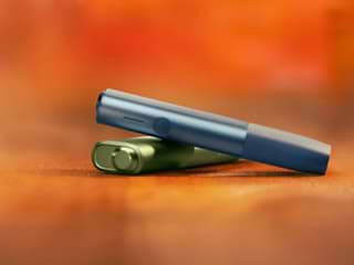 A woman holding an IQOS device looking at a laptop.