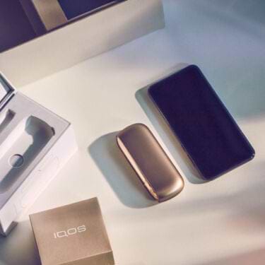 A gold IQOS device out of his packaging, accessories and a mobile on a table