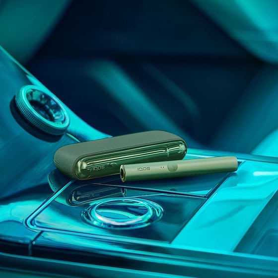 A man holding an obsidian black IQOS ILUMA PRIME Holder while looking at his mobile phone.