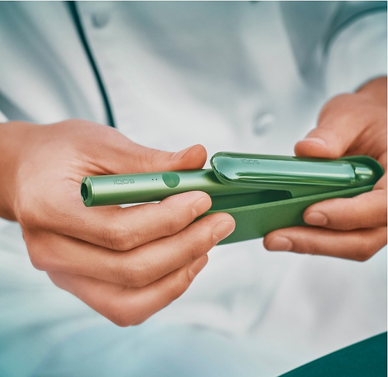 A person holding a smart phone sitting next to a person holding an IQOS device.