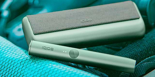 Hands holding smartphones and one IQOS device.