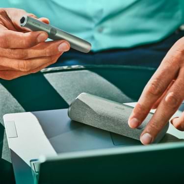 A man's hands opening a mid azure blue IQOS ILUMA device.