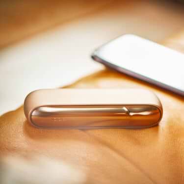 A gold IQOS DUO and a mobile on a couch