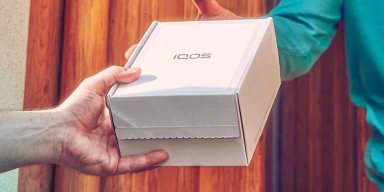 Hands holding an unopened IQOS device box.