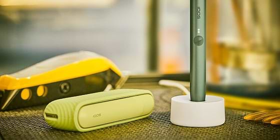 An IQOS ILUMA device in a charging station with a Pocket Charger on a table.