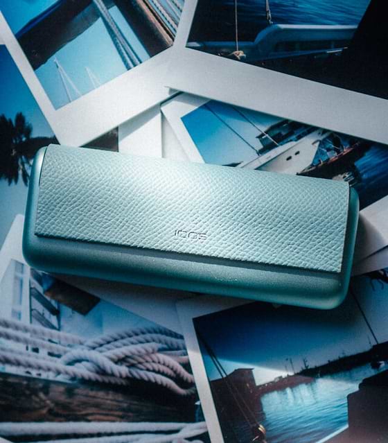 Travel documents, a mobile phone and an IQOS ILUMA PRIME Holder and Pocket Charger on a table.