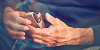 A woman holding an IQOS device looking at a laptop.