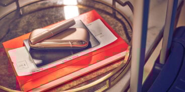 Blond woman checking her phone with a IQOS device on the table and a handbag next to her