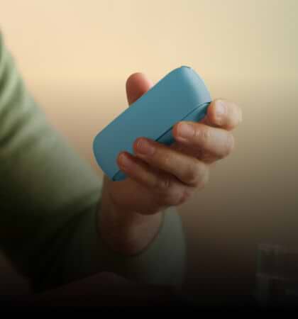 IQOS Originals Duo Holder and Pocket Charger in turquoise color on a desk, next to notebooks.	 	 	