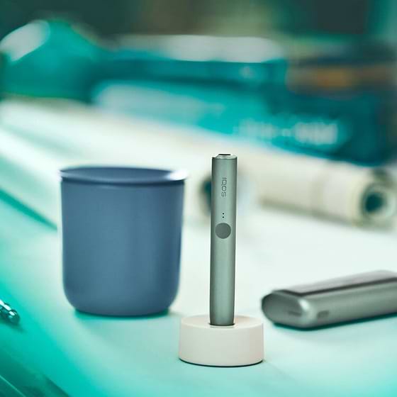 A jade green IQOS ILUMA device next to a blue cup.