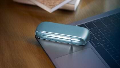 Laptop next to turquoise IQOS ORIGINALS DUO pocket charger.	 	 	