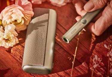 IQOS ILUMA prime device in gold khaki, set on a flower stall.