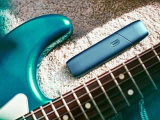 IQOS Originals One heated tobacco device, next to a turquoise guitar.	 	 