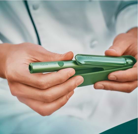 A person holding a smart phone sitting next to a person holding an IQOS device.