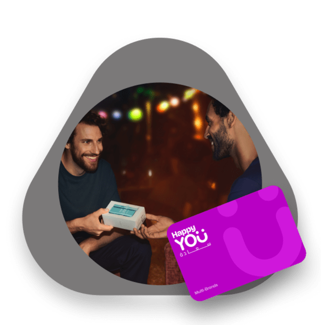 رجلان مبتسمان يتبادلان علبة هدية من آيكوس باللون الفيروزي، مع بطاقة هابي يو البنفسجية في المقدمة.