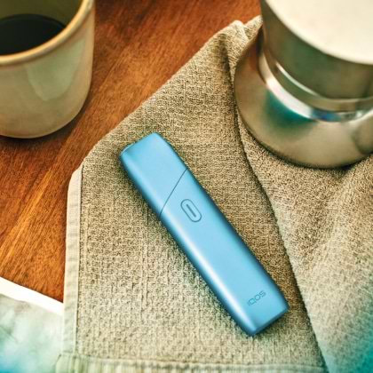 Turquoise IQOS Originals One heated tobacco device on a fabric table mat.	 	 	