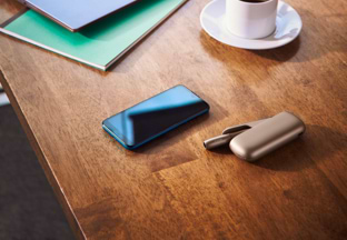 A gold IQOS, a mobile and a cup of coffee on a wooden table.
