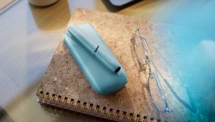 Hands holding IQOS Originals Duo heated tobacco holder and pocket charger in turquoise color.	 	 	